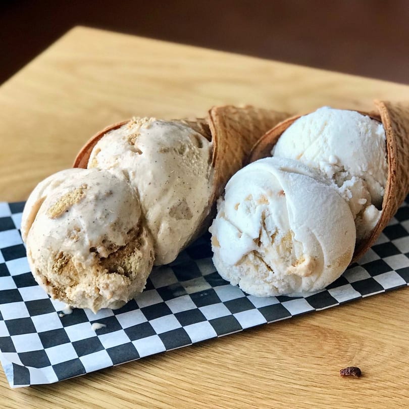 Two waffle cones filled with scoops of Grand Ole Creamery ice cream on a checkered paper.